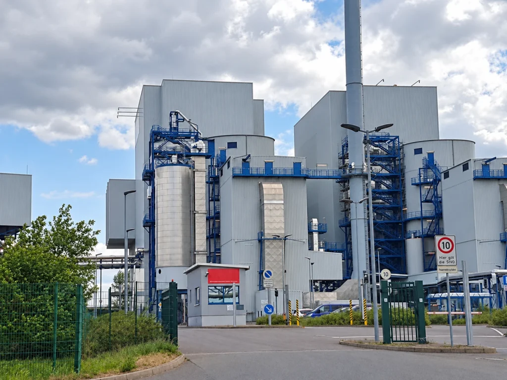 Außenansicht einer industriellen Anlage mit Gebäuden, Stahlbühnen, Rohrleitungen und Treppenkonstruktionen.