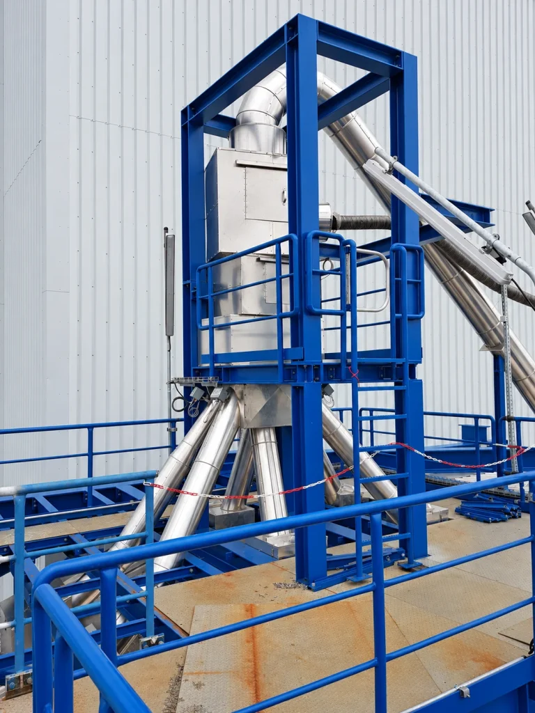 Obere Baugruppen einer Kugelregenanlage mit angeschlossenen Leitungen in einer blauen Stahlkonstruktion mit Wartungsplattform.